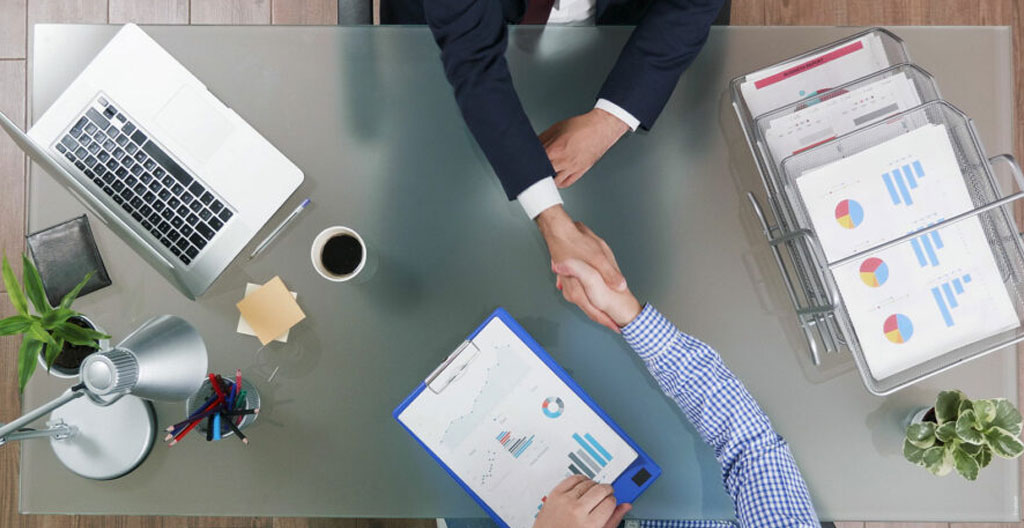 Mains adultes feuilletant un rapport de financement responsable posé sur un bureau en bois clair, lumière naturelle douce